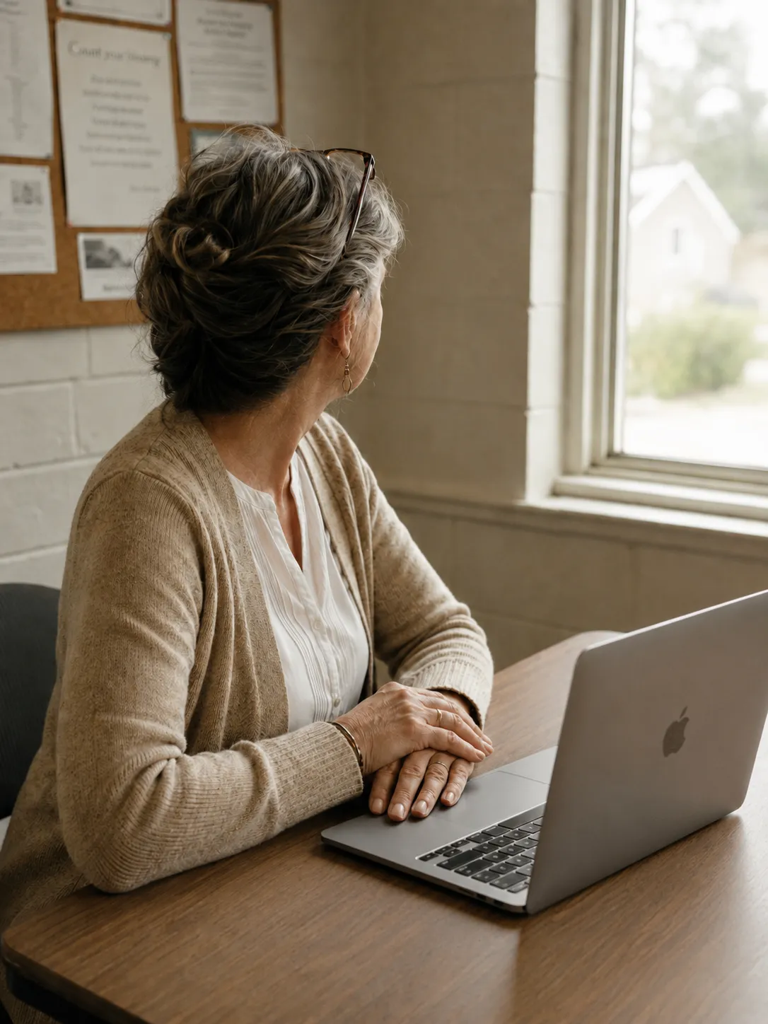 A church finance volunteer at a plain table with a laptop, hands resting, looking out the window